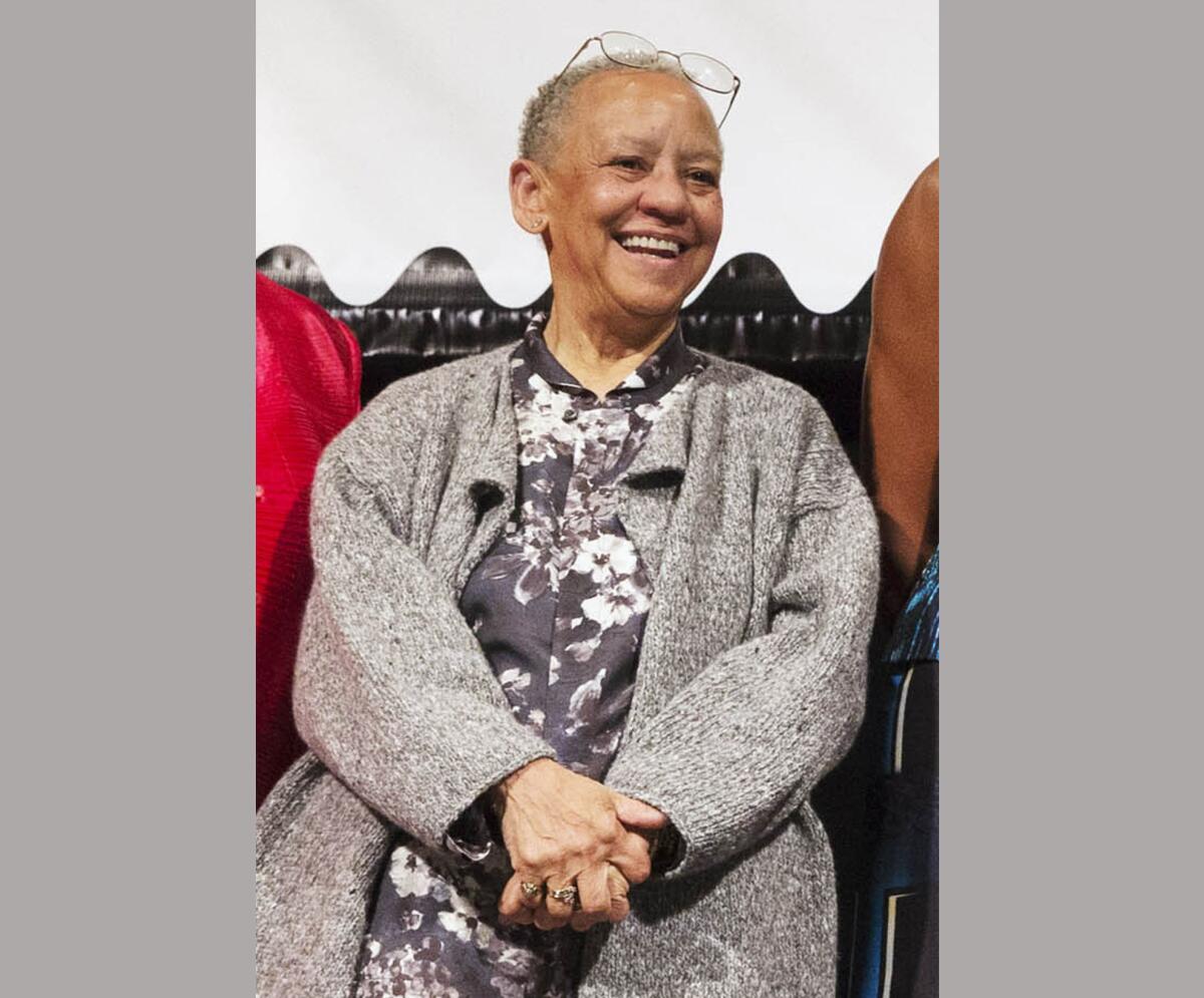  Nikki Giovanni smiles broadly while standing with her hands clasped in front of her