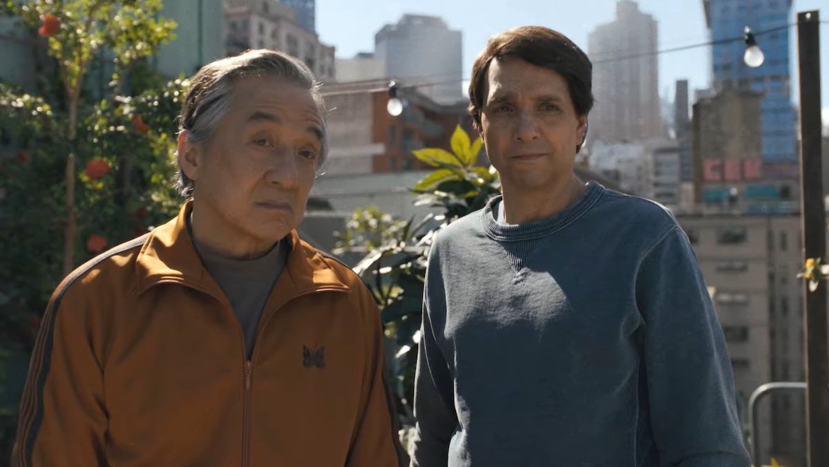 Jackie Chan in an orange jacket and Ralp Macchio in a blue shirt stand on a rooftop in Karate Kid: Legends