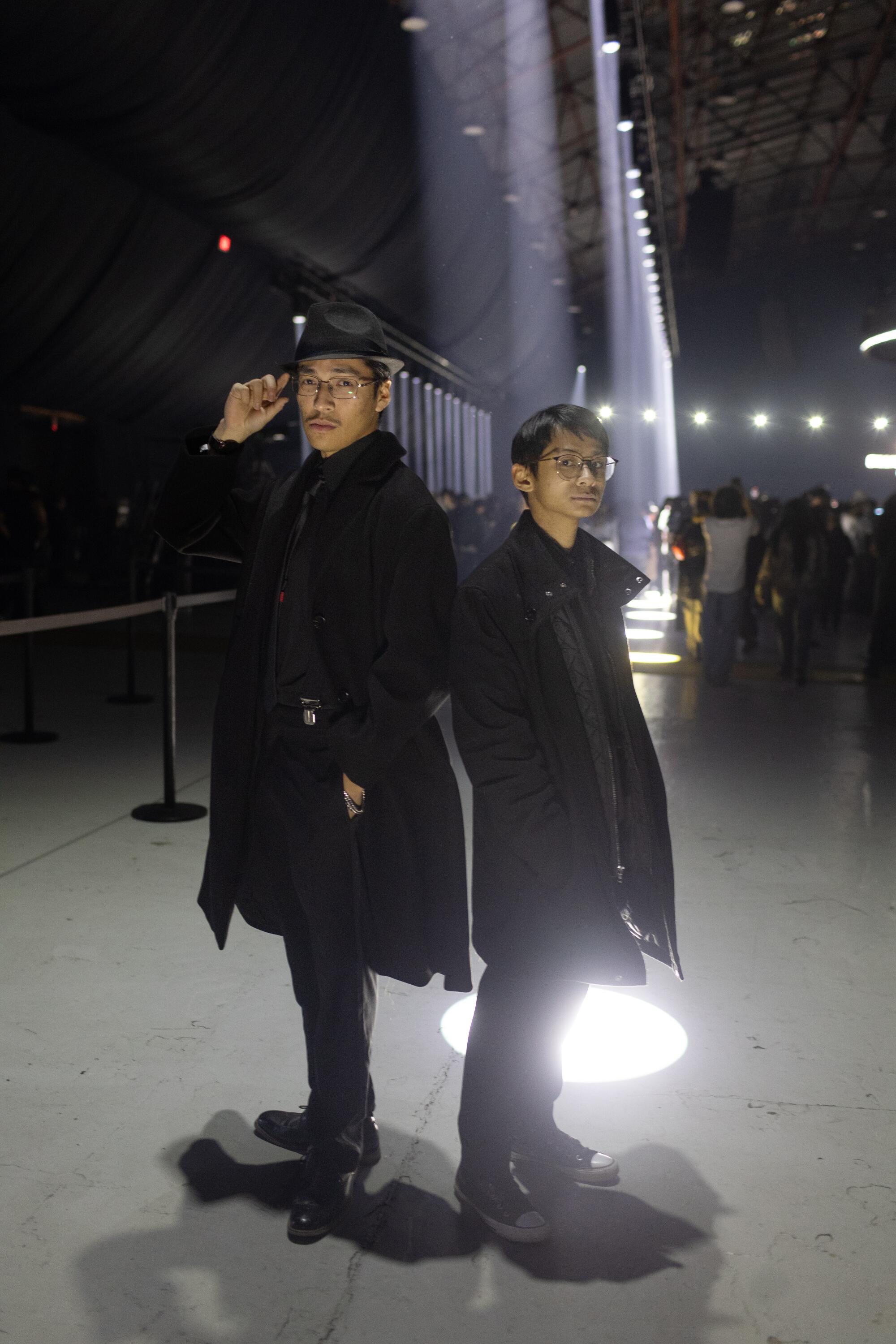 Elijah Shen Muralles, 21, and Cole Dizon, 20, poise in dark coats outdoors at night.