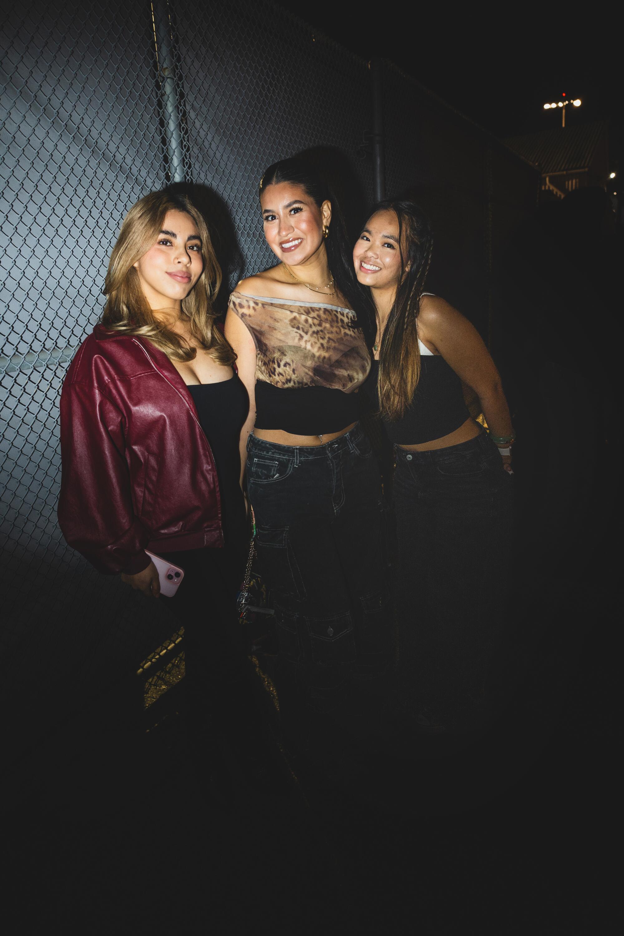 America Maldonado, Maya Garcia and Kessai Suksanguan pose for a photo in front of a fence at night