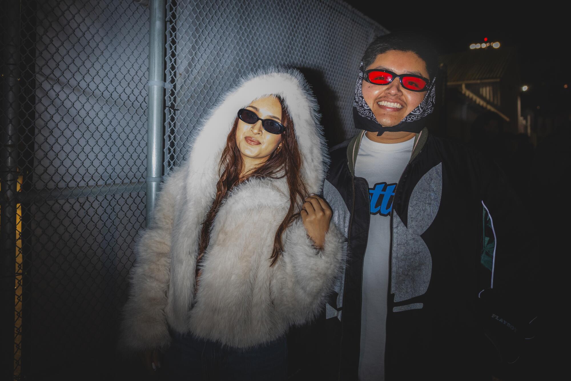 Carmen Flores and Marco De La Cruz pose outdoors at night in front of a fence.