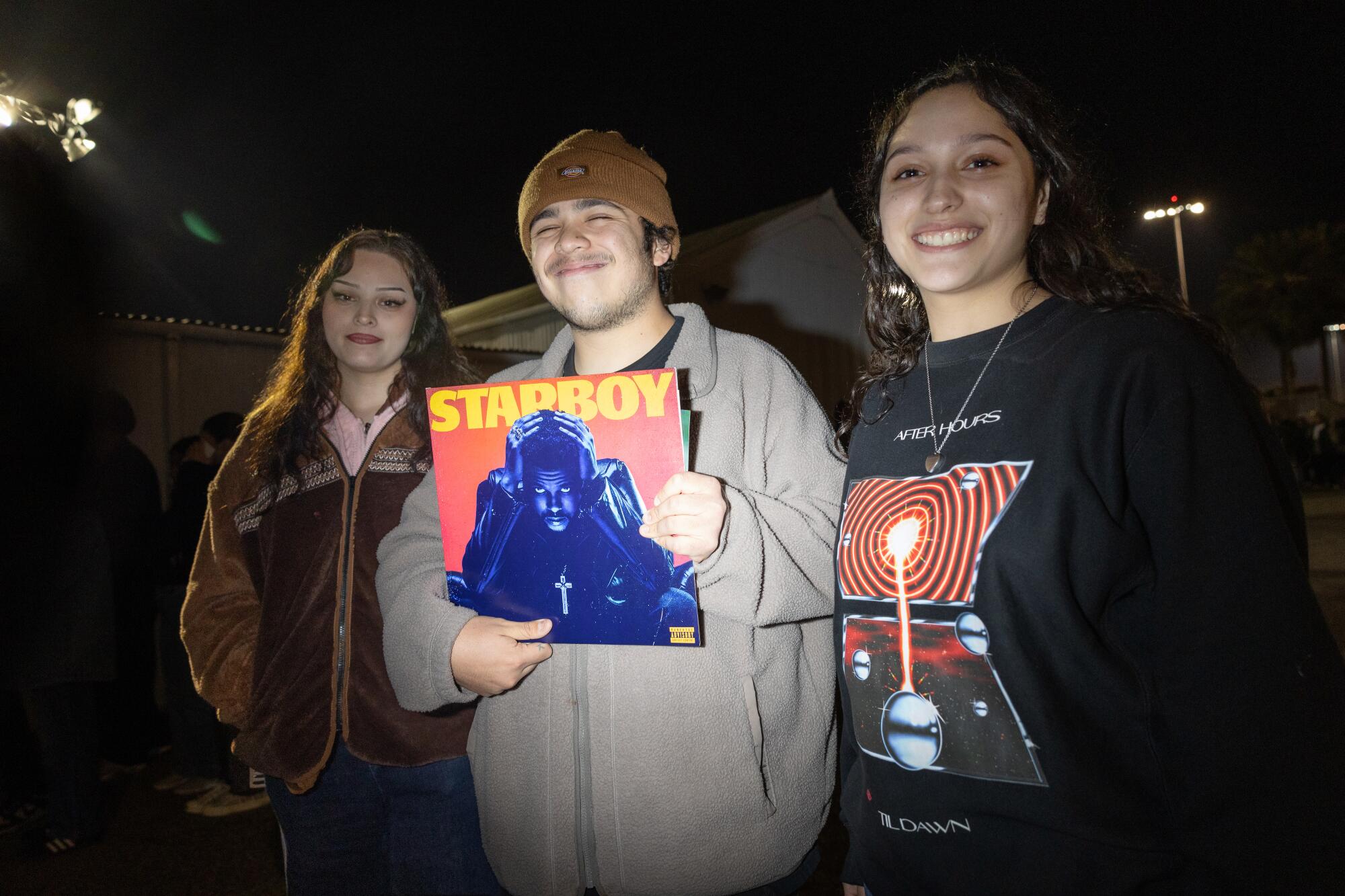 Katherine Martinez, Jorge Martinez holding an album cover and Angelina Bomar outside in the dark.