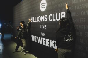 Fans  pose in front of a wall with the words "Billions Club live with the Weeknd."