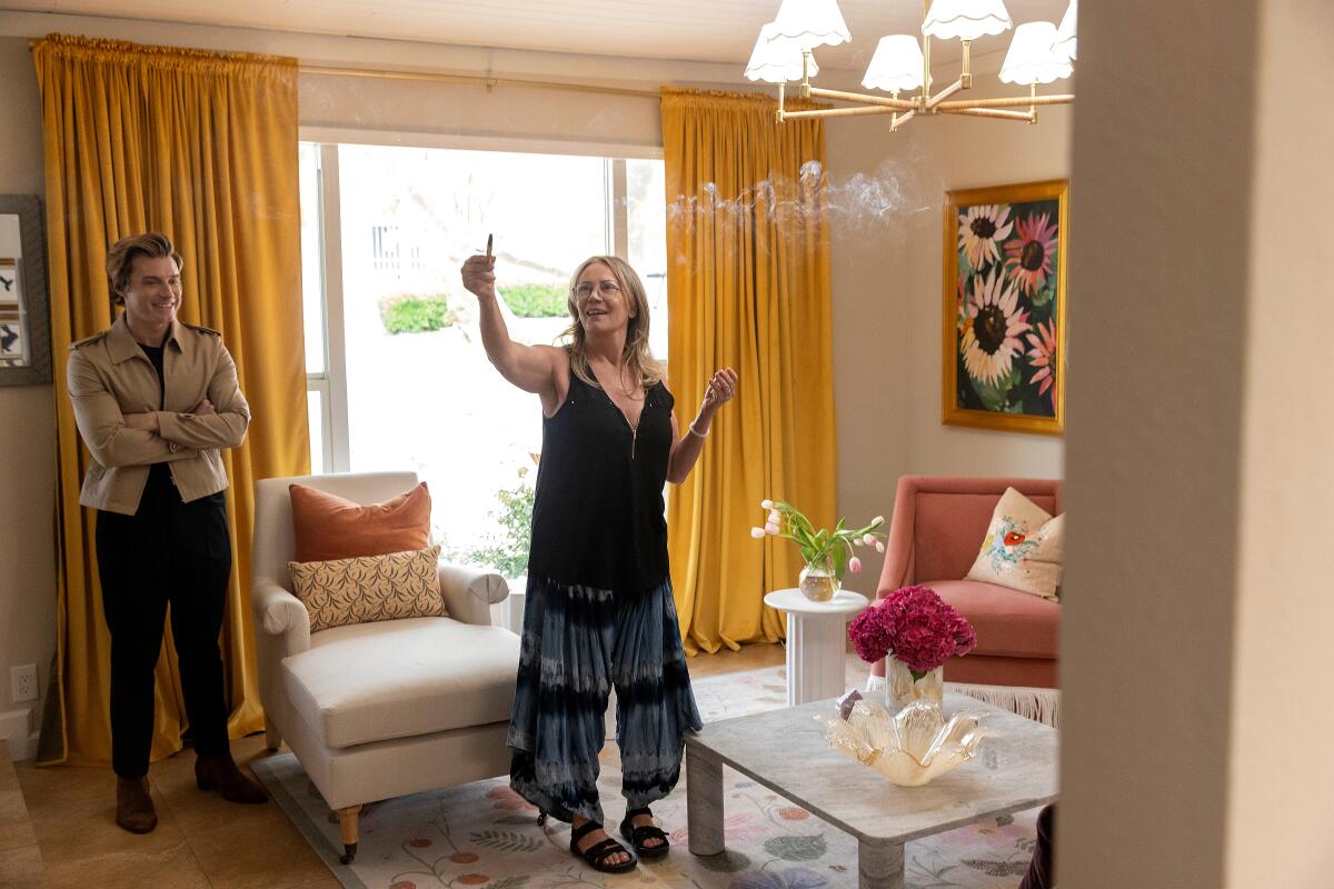 A man watches as a woman, her right arm outstretched to the sky, takes in her renovated living room.