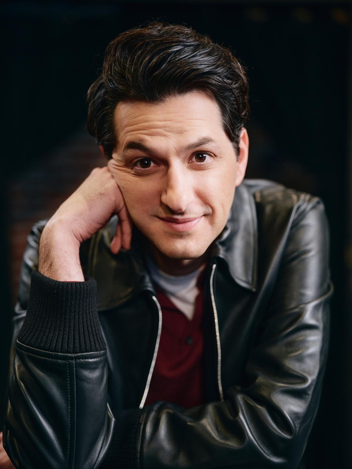 Ben Schwartz wears a leather jacket and rests his face on a hand.