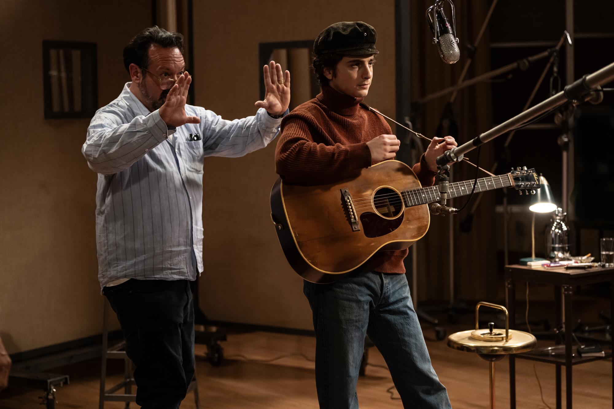 Two men, one with hands raised and the other holding a guitar on the set of "A Complete Unknown."