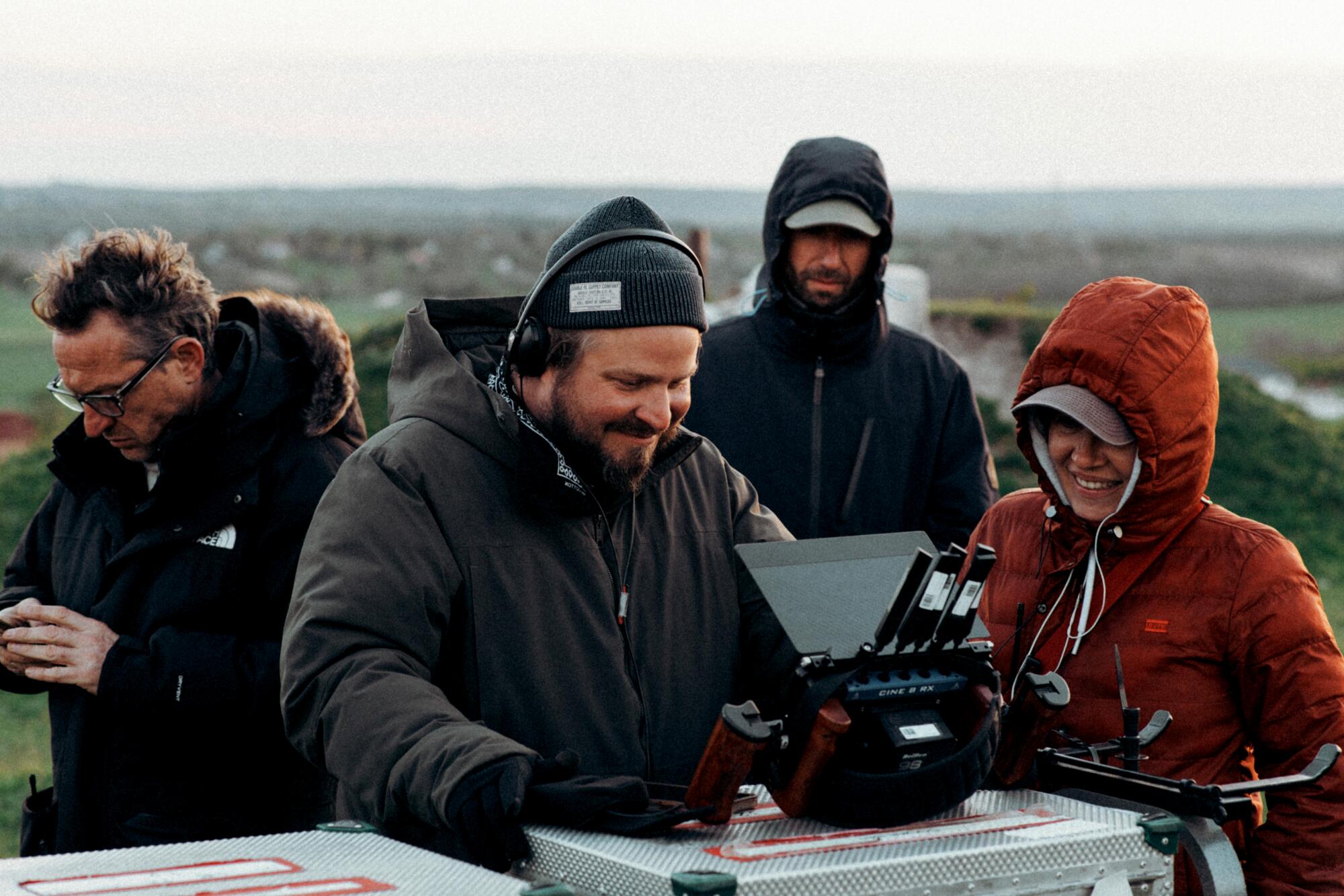 Brady Corbet looks at a video monitor on a film set as others look on.