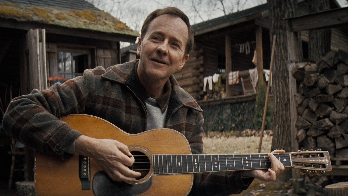 Edward Norton as pete seeger playing a guitar outside in A Complete Unknown