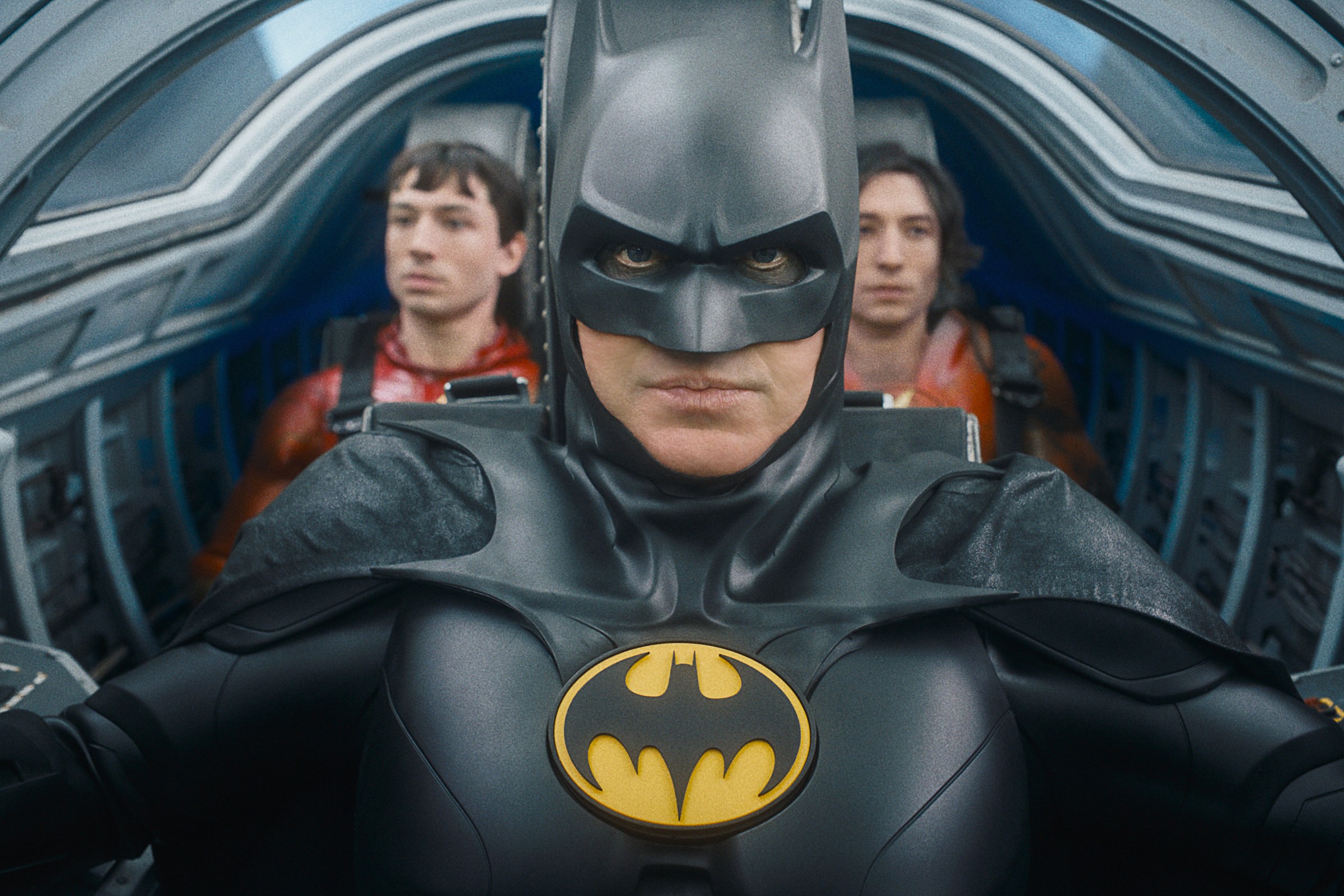 (L-R) Ezra Miller as The Flash, Michael Keaton as Batman and Ezra Miller as The Flash in The Flash. They’re in the cramped cockpit of the Batwing, with Batman in the pilot’s seat and the two Flashes sitting next to each other behind him.