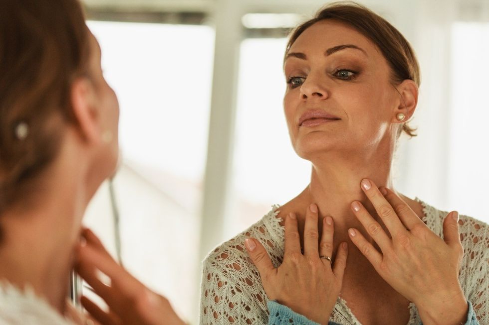 A woman checking her wrinkles and age spots on her skin of her neck in front of a mirror