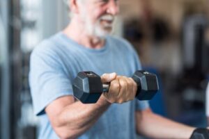 Close up of mature man holding two dumbbells doing exercise at the gym