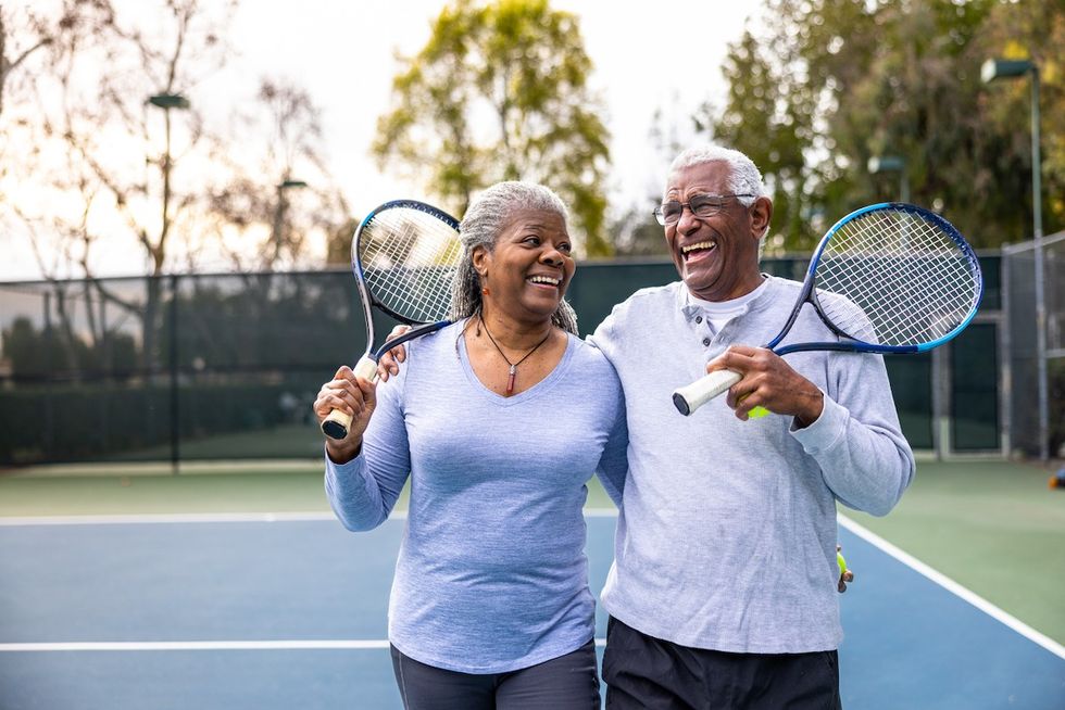 A senior couple laughing and smiling, leaving the tennis court after their workout