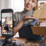 A smartphone films a young woman unpacking a cardboard box