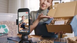 A smartphone films a young woman unpacking a cardboard box