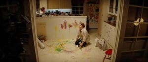 Mother (Amy Adams) kneels in her kitchen looking exhausted, trying to clean up smeared fingerpaints and child handprints in Nightbitch