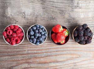 Berries lined up in bowls on wood surface