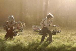 Neel (Robert Timothy Smith), a blue elephant-like alien kid, and Wim (Ravi Cabot-Conyers) push their hoverbikes in a still from Skeleton Crew