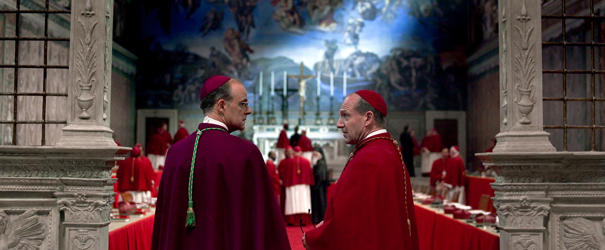 Two men in Catholic robes talk within a decorated chapel in "Conclave."