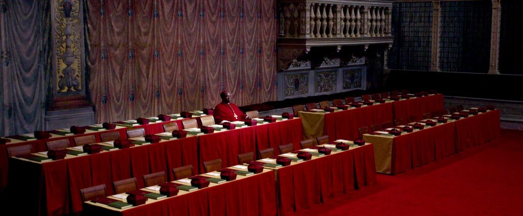 A lone cardinal sits at a long row of red-draped tables in "Conclave."