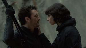 Miles Teller and Anya-Taylor Joy wear all black and embrace in the wilderness in a still from The Gorge movie