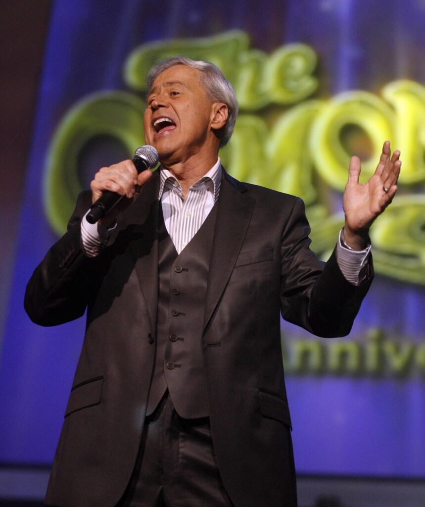 Wayne Osmond sings into a microphone on a stage