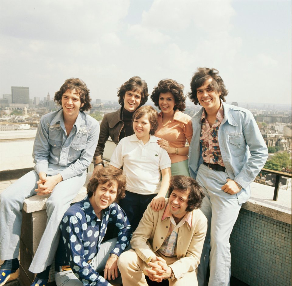 A group portrait of the Osmonds, including Merrill (back, left), Donny, Marie, Jay, Alan, Jimmy, and Wayne (bottom, right) in London