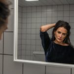 A woman runs her hand through her hair, looking in the mirror.