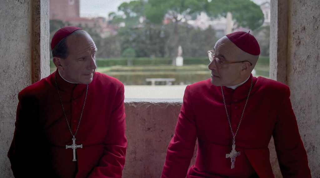 Two cardinals dressed in red discuss papal matters.