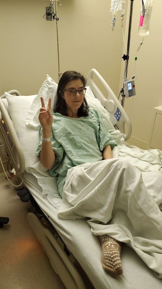 Woman in a hospital bed giving a peace sign.