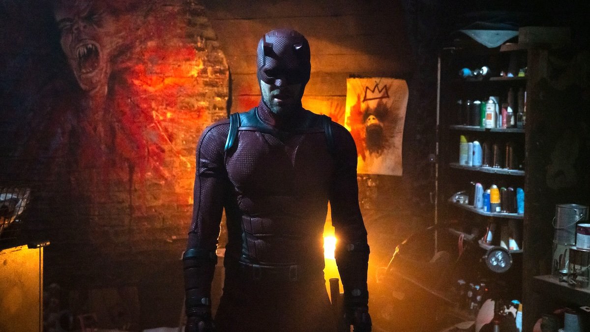 Daredevil stands in a dimly lit cellar with demonic images 