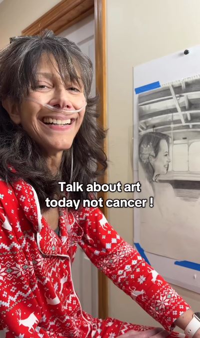 Woman in red pajamas with nasal cannula, smiling and showing a charcoal drawing.