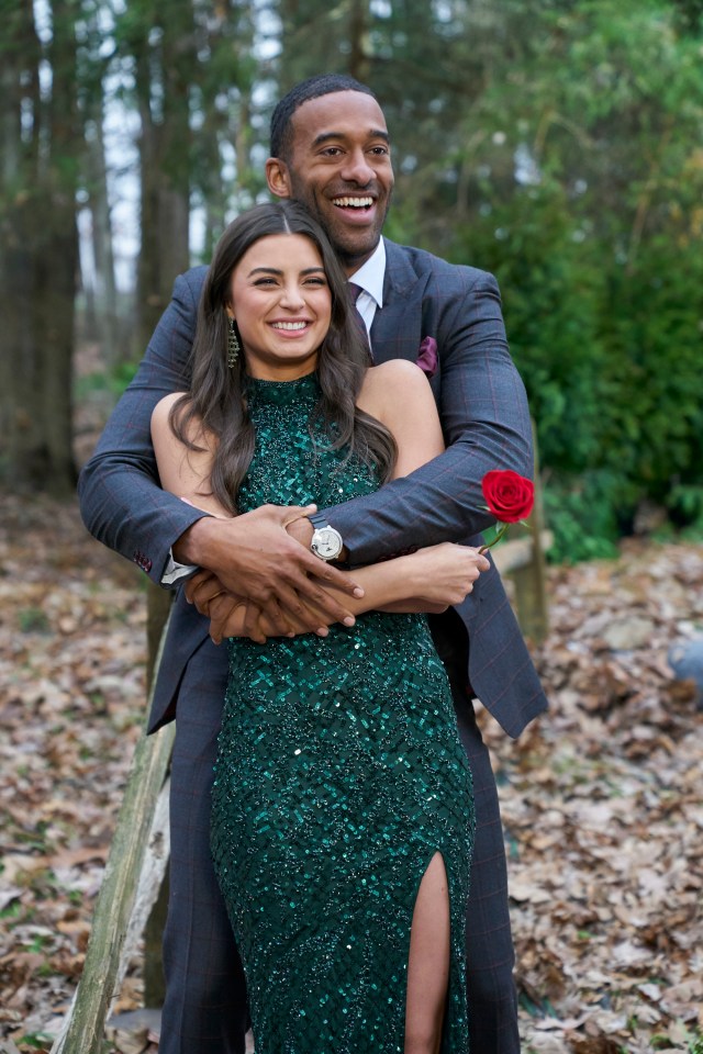 A man and woman embrace, the woman holding a single red rose.