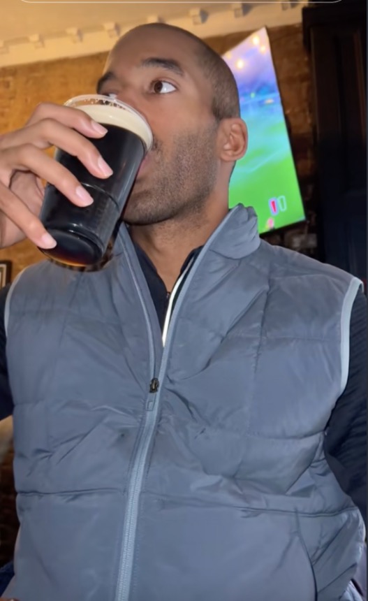 Man in vest drinking from a cup.