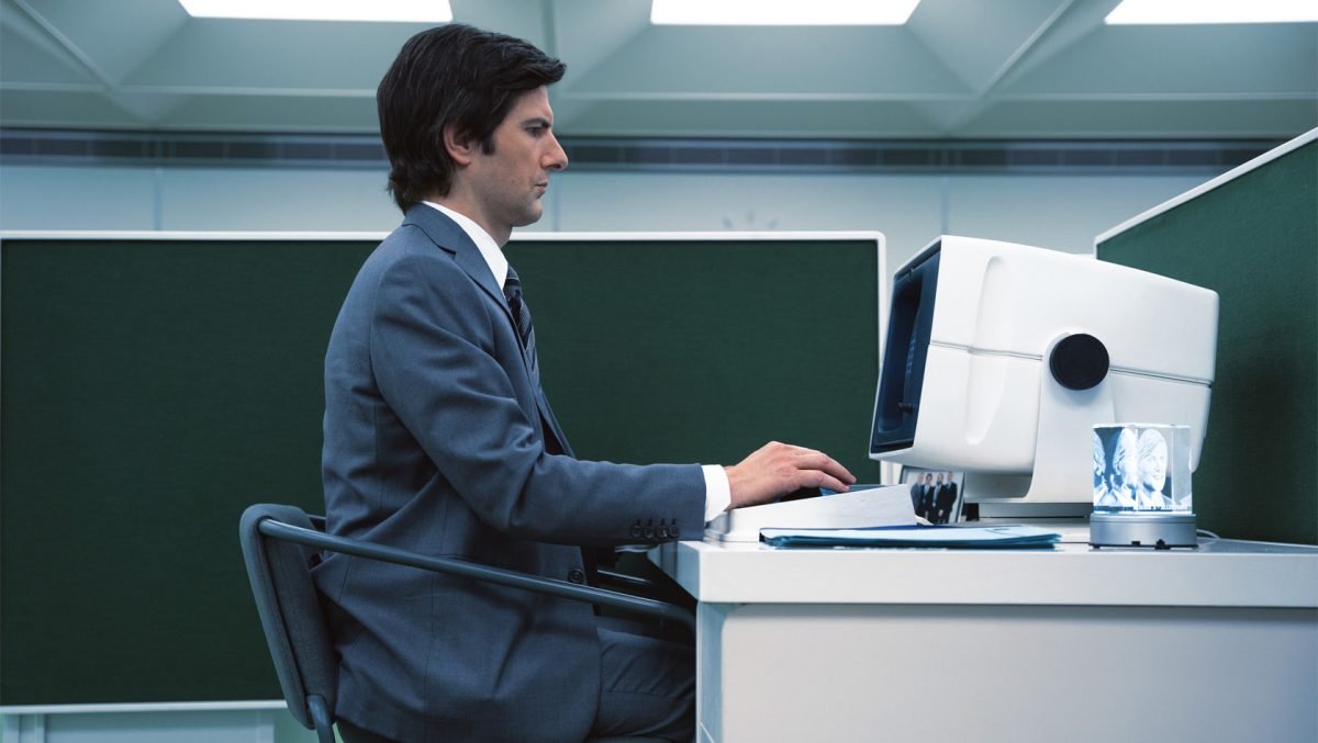 Adam Scott in a suit working at a computer in profile on Severance