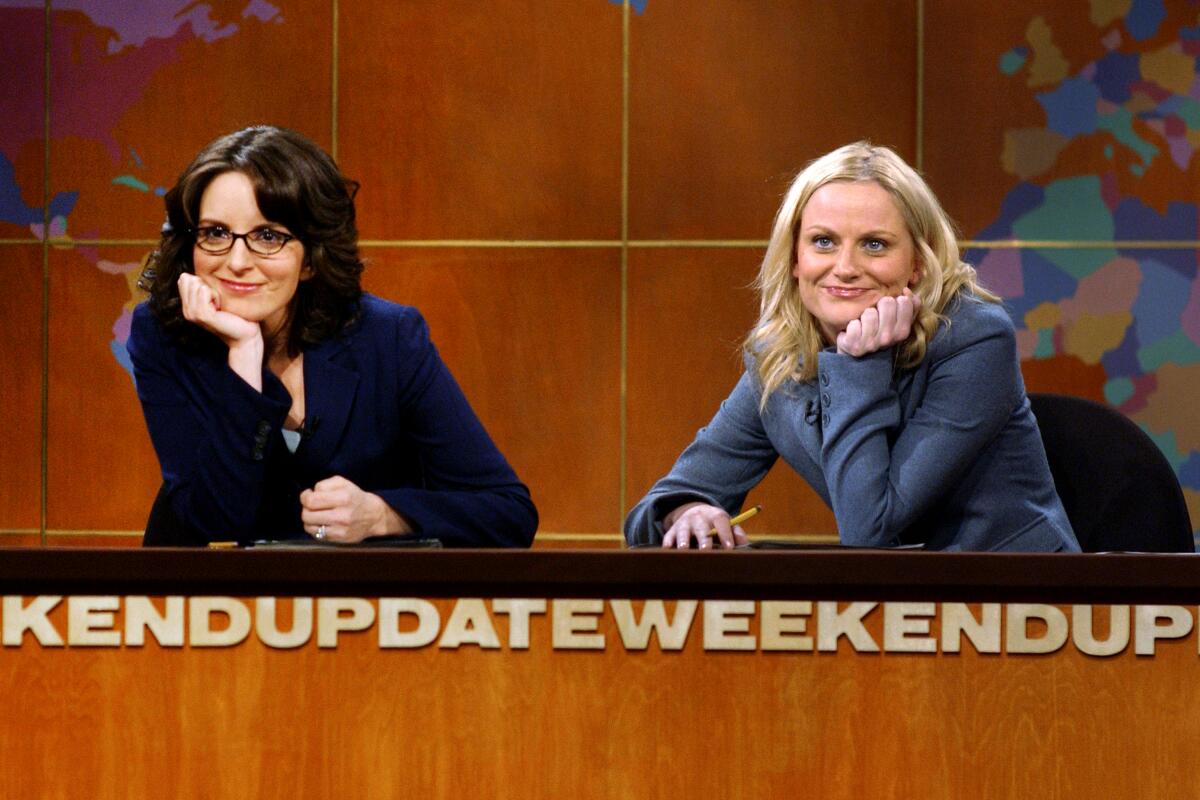 Two women in suits hold their chins in their hands while leaning on a news anchor desk.