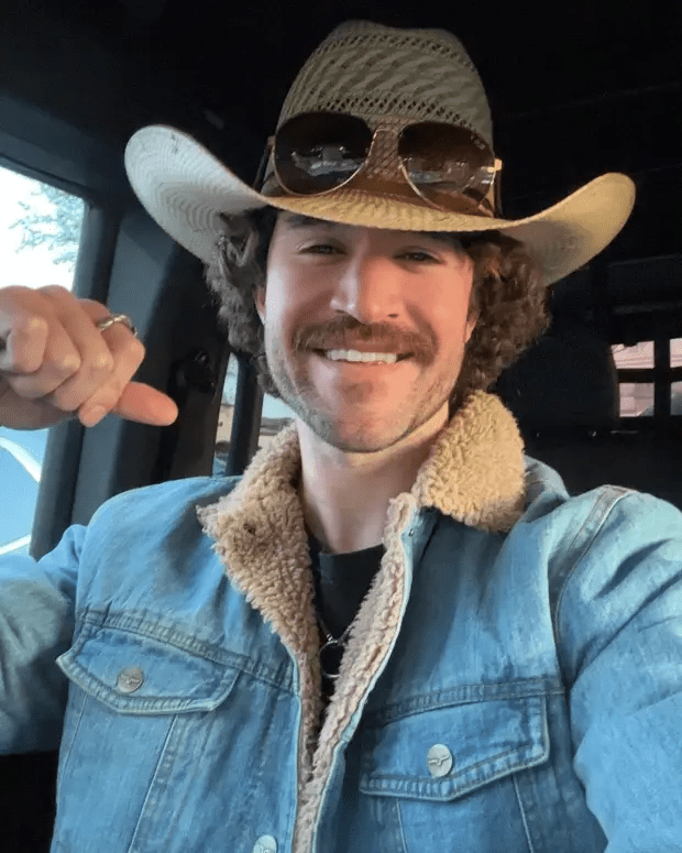 Man in cowboy hat and denim jacket giving a thumbs up.