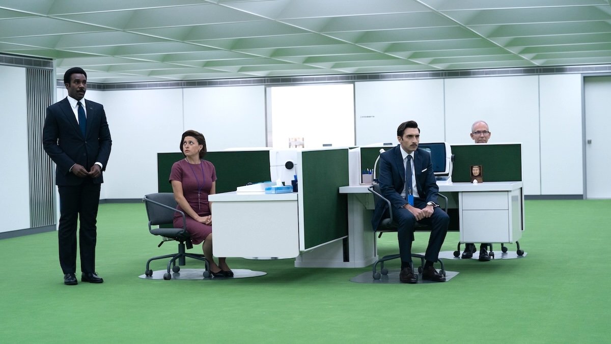 A man standing in an office as three people sit at cramped desks on Severance