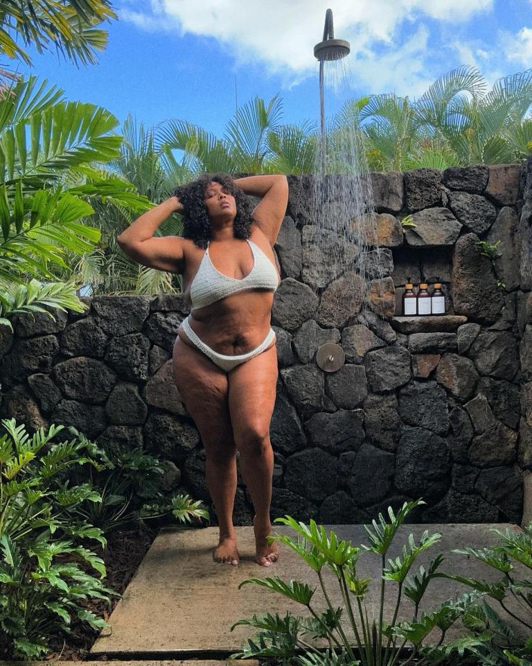 Lizzo in a white bikini showering outdoors.