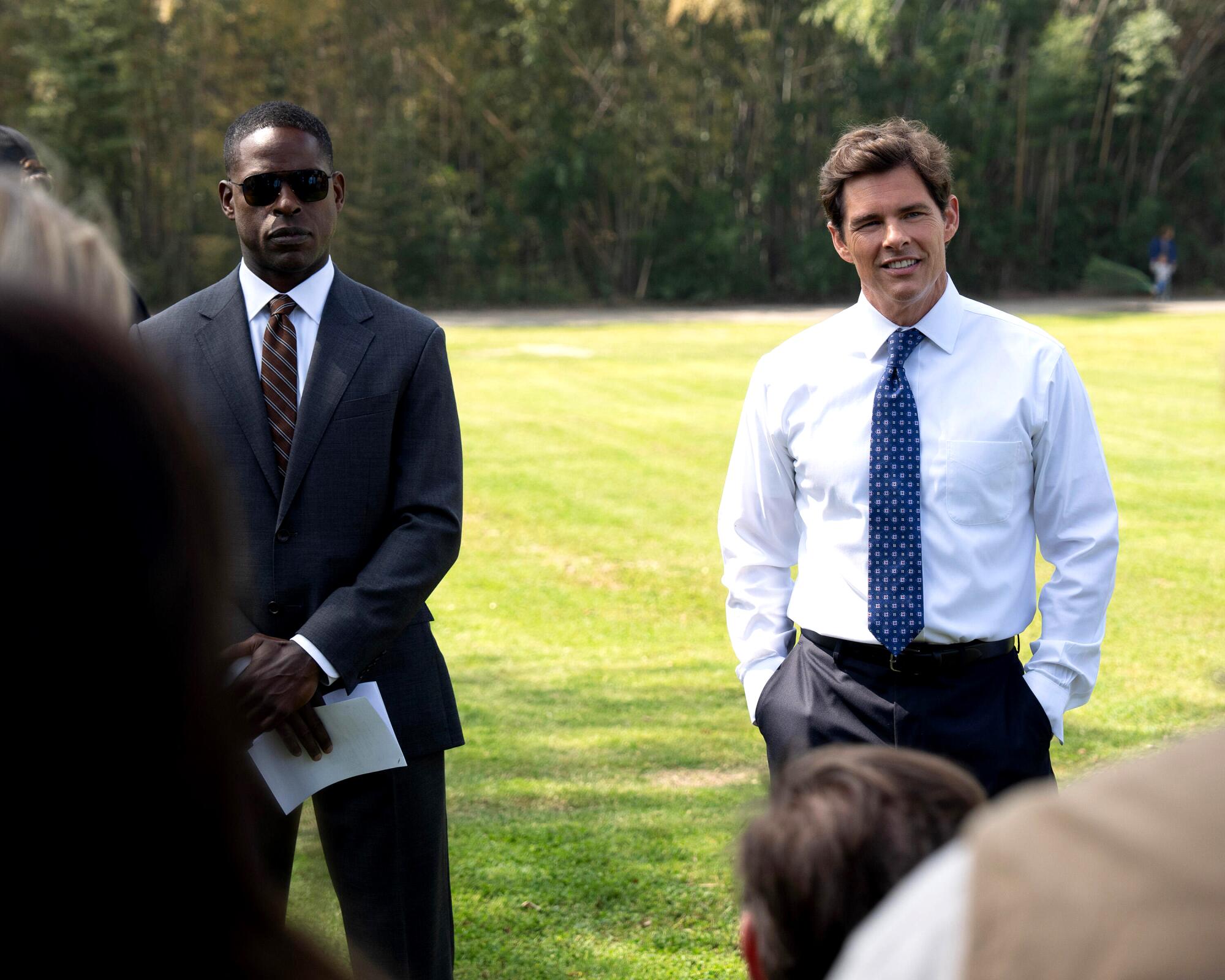 Two men in suit wear stand side by side on a lawn