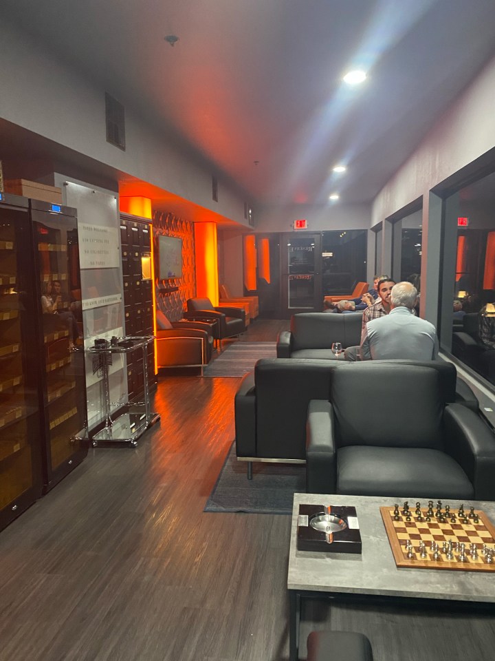 Interior of a cigar lounge with seating, a humidor, and a chessboard.