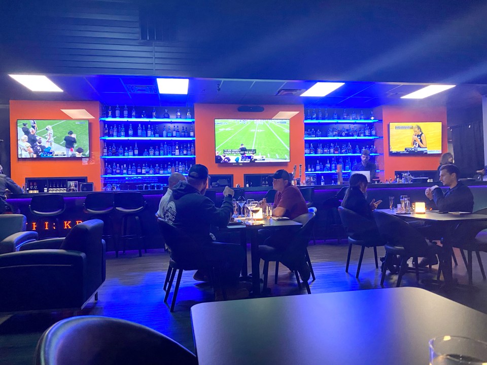 Patrons dining in a dimly lit restaurant with multiple TVs showing sporting events.