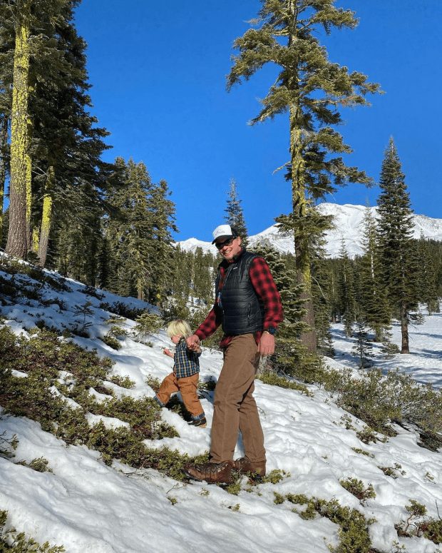 Man and toddler walking in snowy woods.