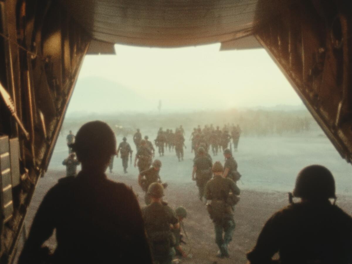 Soldiers wearing helmets exit through the back of an airplane onto a field.