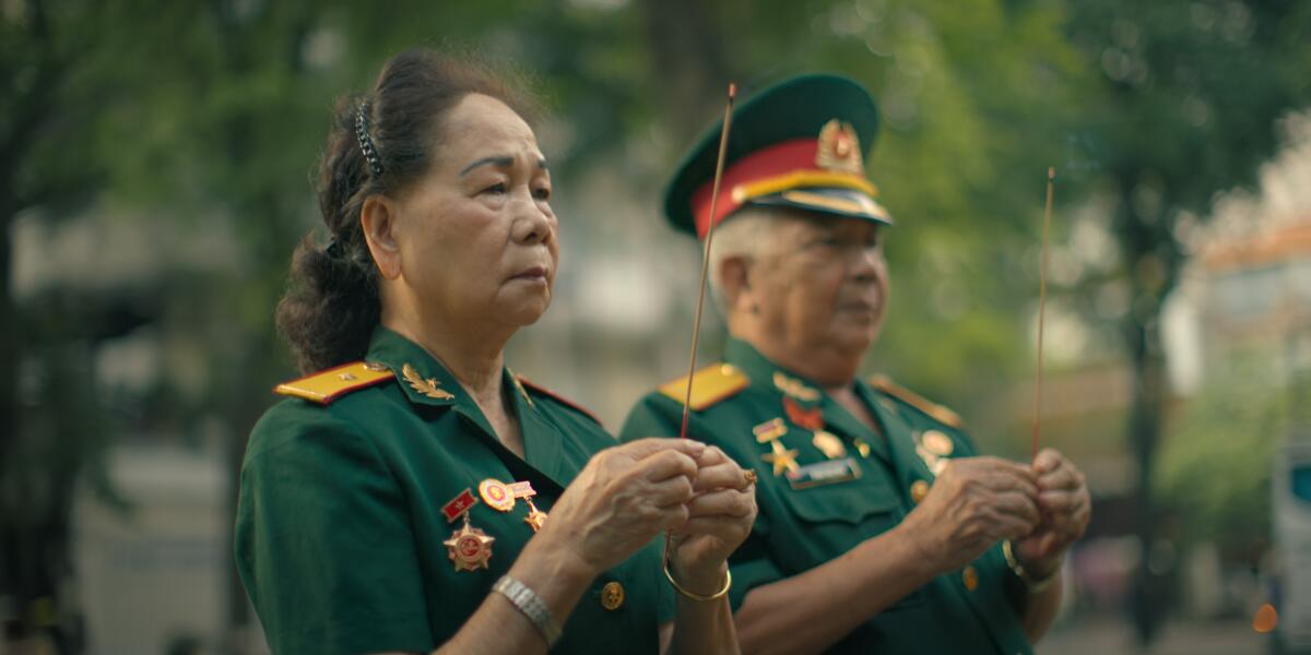 A woman and a man in military uniform holding a stick of incense.