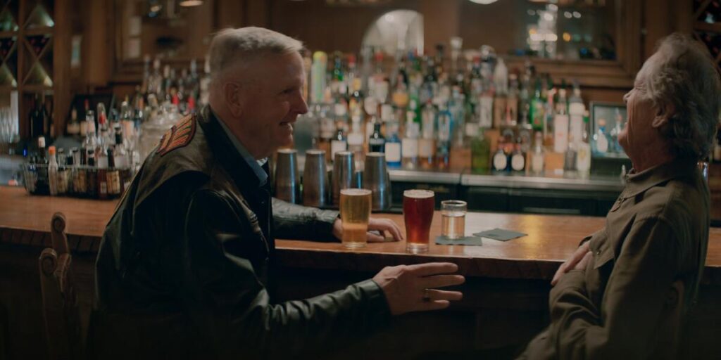 Two men at a bar with beers laughing.