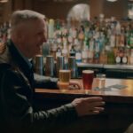 Two men at a bar with beers laughing.