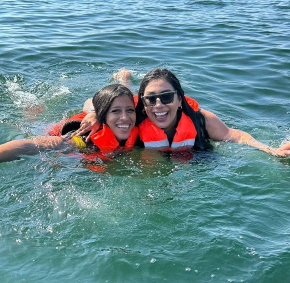 Two women wearing life vests float in the water.