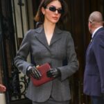 Kendall Jenner wearing a gray suit, sunglasses, and gloves while carrying a burgundy clutch.