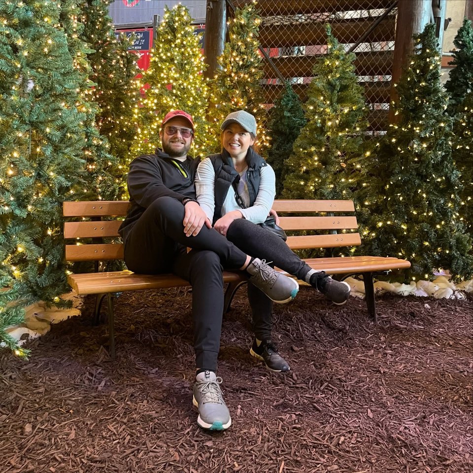 Couple sitting on a bench surrounded by Christmas trees.