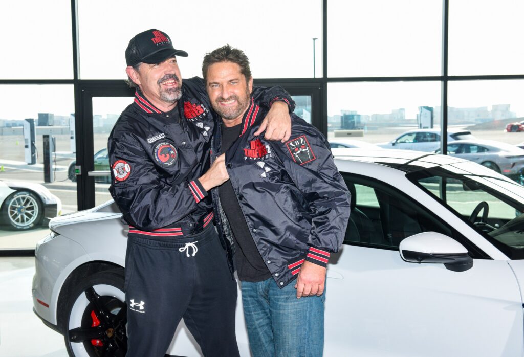 Christian Gudegast and Gerard Butler smile while posing with a Porsche Taycan ahead of their movie Den of Thieves 2: Pantera